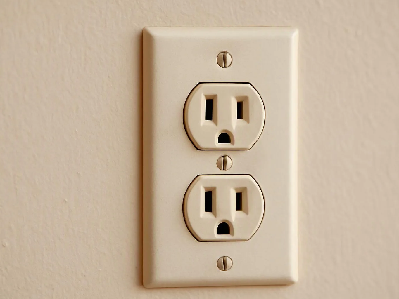 A beige wall outlet with two sockets is mounted on a plain painted wall