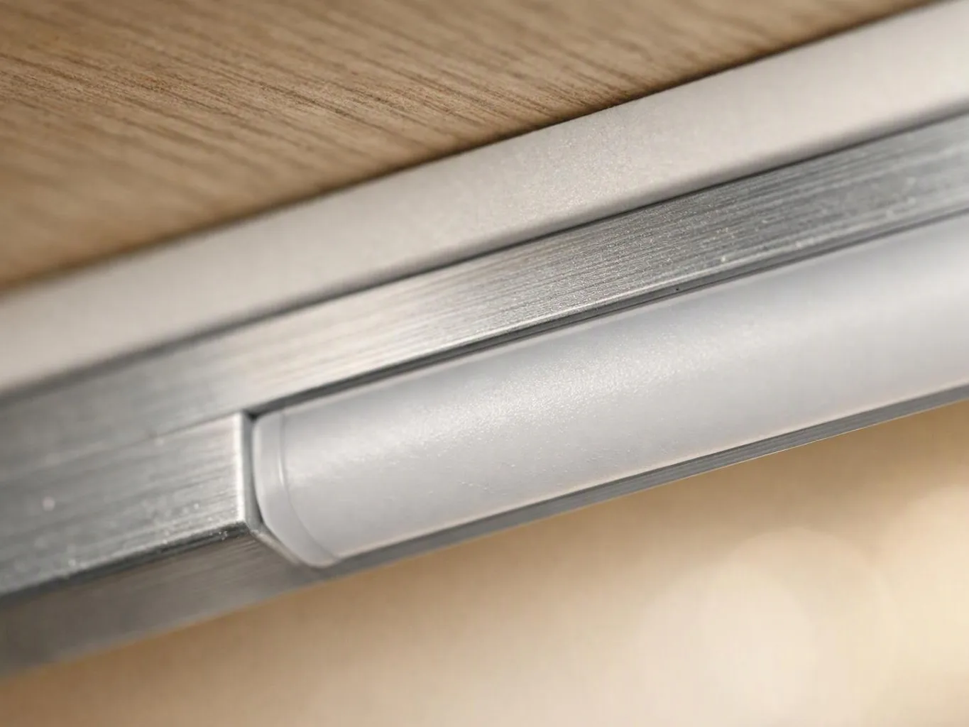 Close-up of a silver metal strip and frosted plastic light fixture mounted under a wooden surface