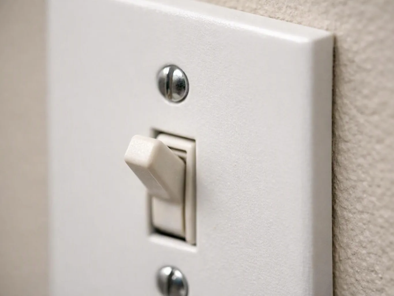 A white light switch sits on a wall, shown in close-up with two screws and a beige toggle
